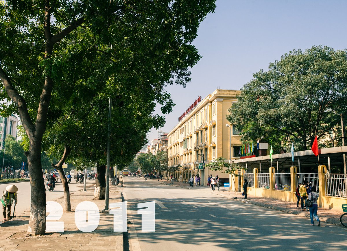 Hình ảnh đường Nguyễn Trãi tại Hà Nội với nhiều cây xanh, người đi bộ và xe máy trên đường. Không khí buổi sáng tạo cảm giác yên bình và nhộn nhịp của cuộc sống đô thị.