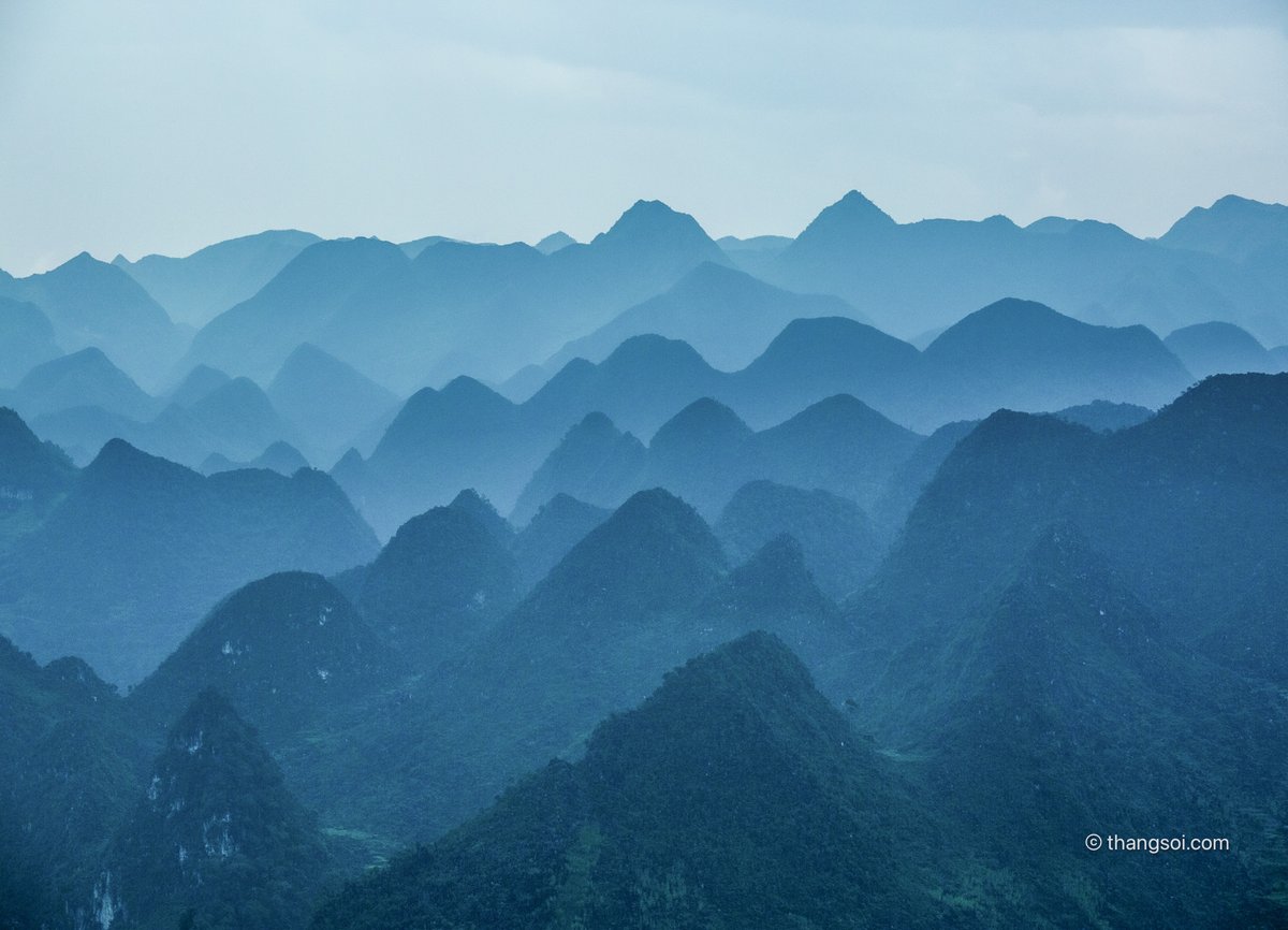 Bức ảnh chụp cảnh cao nguyên đá với các ngọn núi và đồi xanh mờ ảo trong sương mù. Khung cảnh tạo cảm giác bình yên và tĩnh lặng, mang lại sự thư thái cho người xem.