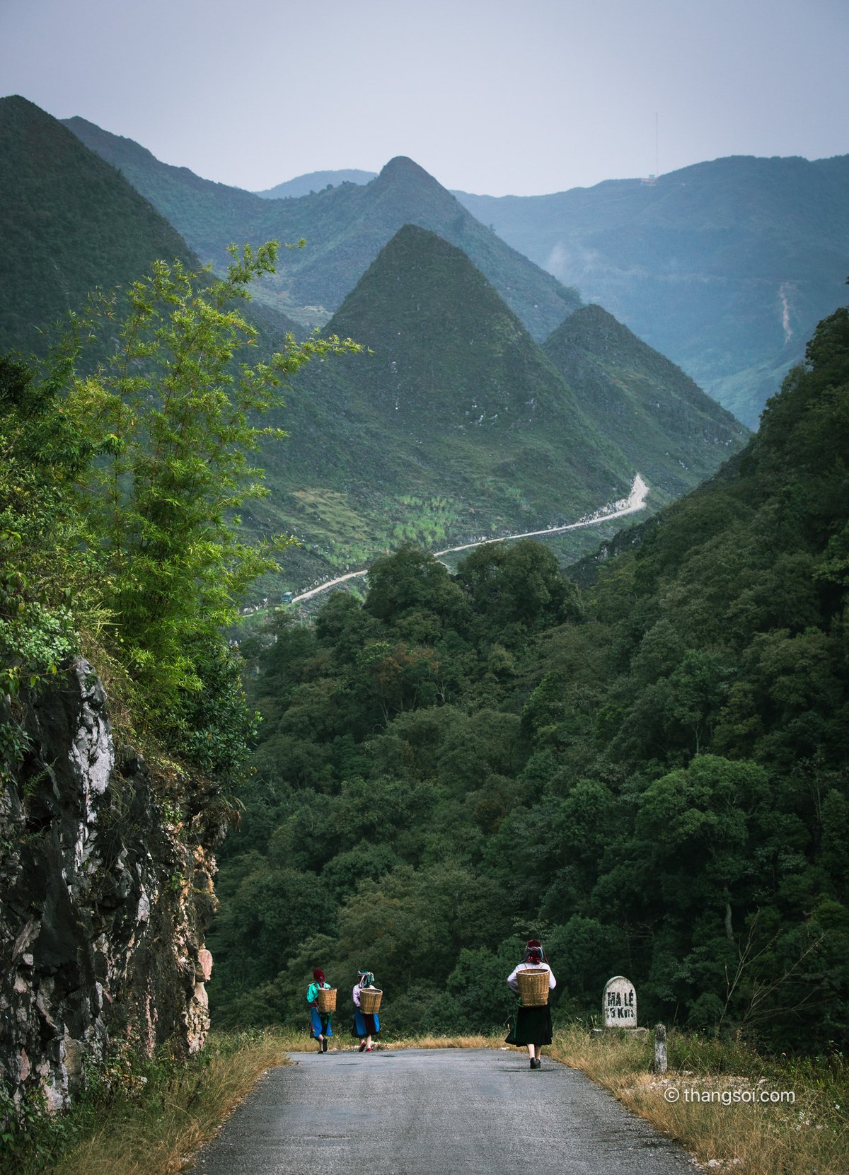 Bức ảnh chụp một con đường nhỏ uốn lượn qua cao nguyên đá với những ngọn núi và rừng xanh bao quanh. Không khí yên bình và tĩnh lặng tạo cảm giác thư thái và gần gũi với thiên nhiên.
