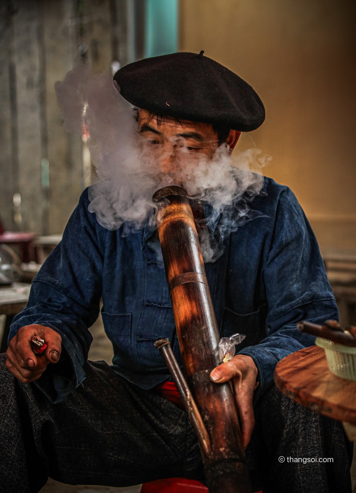 Bức ảnh chụp một người đàn ông đang hút thuốc lào bằng ống tre trong không gian trong nhà. Hình ảnh thể hiện phong tục truyền thống và đời sống thực của người dân vùng cao nguyên đá Việt Nam.