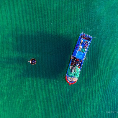 Ảnh chụp từ trên cao cho thấy một chiếc tàu cá và một thuyền thúng trên vùng biển xanh trong. Hình ảnh mang lại cảm giác yên bình và truyền tải hoạt động đánh cá truyền thống của làng chài ven biển.