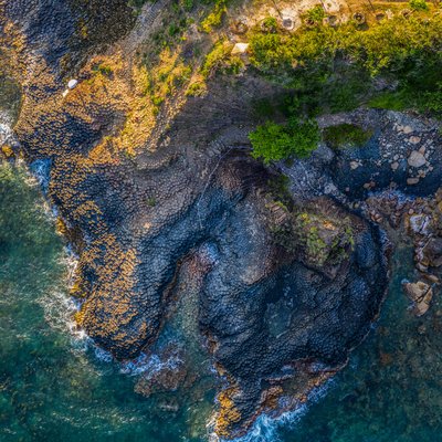 Ảnh chụp từ trên cao cho thấy cảnh quan gành đá đĩa với các khối đá bazan hình lục giác đặc trưng nằm bên bờ biển Phú Yên. Toàn cảnh mang lại cảm giác yên bình và hài hoà giữa thiên nhiên và biển cả.