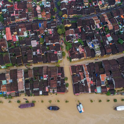 Ảnh chụp toàn cảnh trên không của khu phố cổ Hội An trong mùa lũ với các con đường và sông ngập nước, thuyền neo đậu dọc bờ. Hình ảnh mang đến cảm giác yên bình dù cảnh vật bị ngập lụt, thể hiện sự hoà hợp giữa thiên nhiên và đô thị cổ kính.