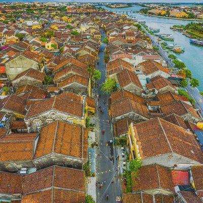 Hình ảnh toàn cảnh trên cao của một phố cổ với các mái ngói đỏ đặc trưng và dòng sông uốn lượn bên cạnh. Cảnh quan mang lại cảm giác yên bình và truyền thống với ánh sáng tự nhiên dịu nhẹ chiếu sáng khắp khu vực.