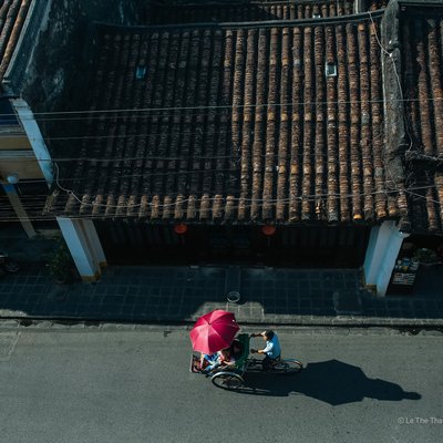 Bức ảnh chụp một chiếc xích lô đang di chuyển trên con phố cổ Hội An dưới ánh sáng tự nhiên ban ngày. Hình ảnh gợi lên cảm giác yên bình và truyền tải nét văn hoá truyền thống đặc trưng của khu phố cổ.