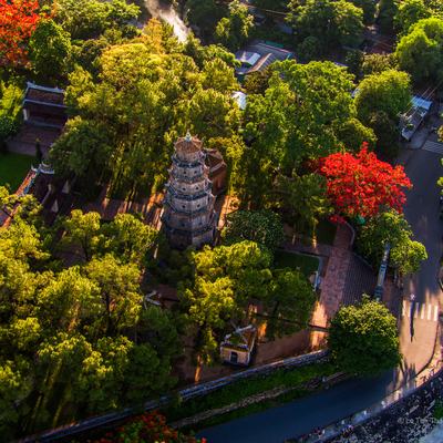 Hình ảnh chụp toàn cảnh trên cao của chùa Thiên Mụ tại Huế với nhiều cây xanh và kiến trúc truyền thống nổi bật. Toàn cảnh mang lại cảm giác yên bình và tĩnh lặng giữa không gian thiên nhiên và di sản văn hoá.