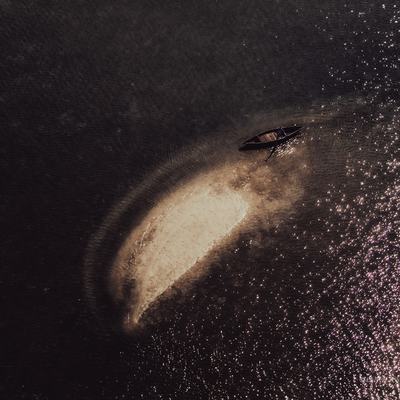 Bức ảnh chụp từ trên cao một chiếc thuyền truyền thống đang chèo trên mặt nước đầm phẳng lặng với ánh sáng tự nhiên dịu nhẹ. Cảnh vật tạo cảm giác yên bình và tĩnh lặng, thể hiện vẻ đẹp giản dị của miền Trung Việt Nam.