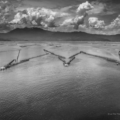 Bức ảnh chụp đầm Cầu Hai ở Huế với cảnh biển rộng lớn, núi non phía xa và những đám mây dày đặc trên bầu trời. Toàn cảnh tạo cảm giác yên bình và tĩnh lặng, thể hiện vẻ đẹp truyền thống của vùng Trung Bộ Việt Nam.