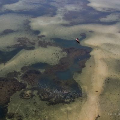 Ảnh chụp toàn cảnh trên không của đầm Lập An với ánh sáng tự nhiên chiếu sáng mặt nước trong xanh và thuyền nhỏ trên đầm. Cảnh quan tạo cảm giác yên bình và tĩnh lặng, thể hiện vẻ đẹp tự nhiên của vùng đầm phá miền Trung.