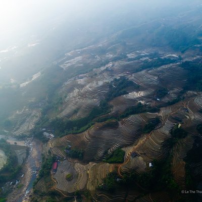 Ảnh chụp từ trên cao cho thấy cánh đồng bậc thang ở Tả Van, với sương mù nhẹ bao phủ và dòng sông chảy qua thung lũng. Khung cảnh mang lại cảm giác yên bình và tĩnh lặng của vùng núi Tây Bắc Việt Nam.