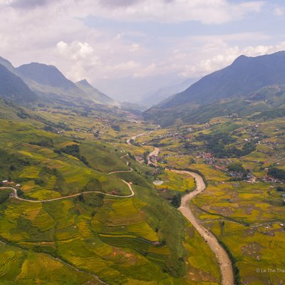 Ảnh chụp thung lũng Tả Van với ruộng bậc thang xanh vàng trải dài bên dòng sông uốn lượn, bao quanh bởi những ngọn núi cao. Cảnh quan tạo cảm giác yên bình và rộng lớn, thể hiện vẻ đẹp tự nhiên của vùng cao nguyên Việt Nam.