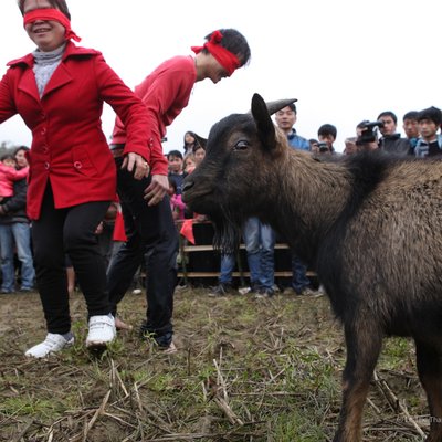 Bức ảnh chụp cảnh một trò chơi truyền thống bịt mắt bắt dê tại lễ hội ngoài trời ở vùng cao nguyên. Không khí sôi động với nhiều người tham gia và khán giả xung quanh tạo nên cảm giác vui tươi, náo nhiệt.