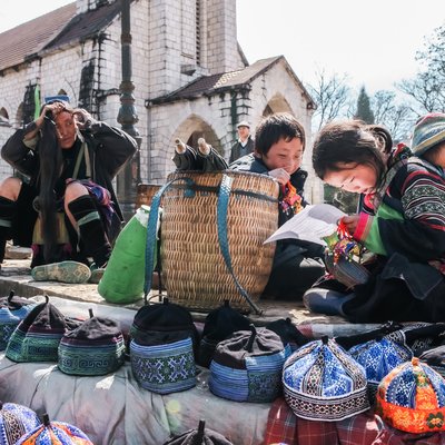 Bức ảnh chụp một nhóm người dân địa phương đang buôn bán mũ truyền thống trước nhà thờ đá tại thị trấn Sapa. Cảnh vật mang lại cảm giác bình yên và chân thực về cuộc sống thường nhật nơi đây.