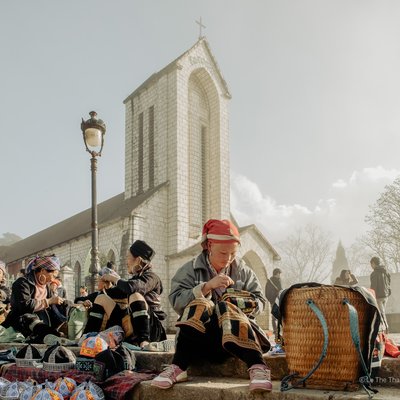 Bức ảnh chụp cảnh chợ ngoài trời gần nhà thờ ở Sa Pa với nhiều người dân tộc thiểu số đang bán hàng thủ công mỹ nghệ. Không khí yên bình và truyền thống hiện rõ qua trang phục và hoạt động của mọi người.