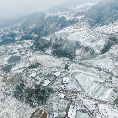 Bức ảnh chụp toàn cảnh khu vực Sa Pa với ruộng bậc thang phủ đầy tuyết trắng và sương mù bao phủ. Cảnh vật mang lại cảm giác yên bình và tĩnh lặng của mùa đông vùng cao nguyên.