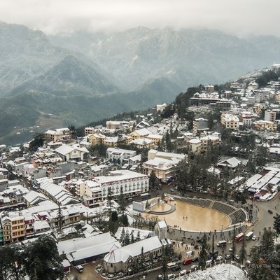 Ảnh chụp toàn cảnh thị trấn Sa Pa nằm trên vùng núi cao với tuyết phủ trắng các mái nhà và cây cối. Khung cảnh mang lại cảm giác yên bình và tĩnh lặng trong mùa đông mờ sương.