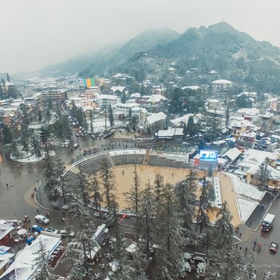 Bức ảnh chụp toàn cảnh thị trấn Sa Pa mùa đông với tuyết phủ trên các mái nhà và con đường quanh co. Khung cảnh mang lại cảm giác yên bình và mờ ảo trong không khí lạnh của mùa đông.