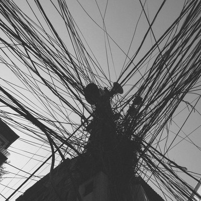 Hình ảnh chụp một cột điện với rất nhiều dây cáp quang và dây điện chằng chịt. Bức ảnh tạo cảm giác hỗn độn và phức tạp trong hệ thống dây điện đô thị.