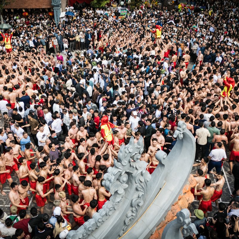 Hình ảnh một đám đông lớn người tham gia lễ hội truyền thống tại Đồng Kỵ, nhiều người đàn ông mặc quần đỏ và không áo đang tụ tập. Không khí lễ hội rất sôi động và náo nhiệt, thể hiện sự gắn kết cộng đồng mạnh mẽ.