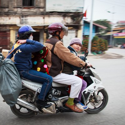 Bức ảnh chụp một gia đình gồm bốn người đang di chuyển trên một chiếc xe máy chở nhiều đồ đạc trên đường phố. Hình ảnh thể hiện sự nhộn nhịp và cảm giác ấm áp của việc trở về quê ăn Tết trong đời sống hàng ngày.