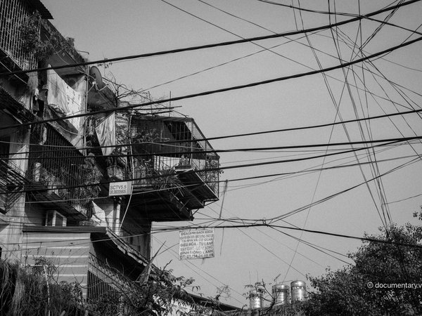 Bức ảnh chụp một phần của nhà tập thể với các chuồng cọp được cơi nới và nhiều dây điện chằng chịt phía trước. Hình ảnh gợi lên cảm giác hoài niệm về cuộc sống đô thị truyền thống ở Hà Nội.