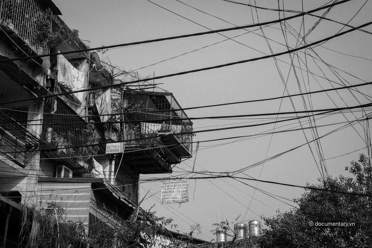 Bức ảnh chụp một phần của nhà tập thể với các chuồng cọp được cơi nới và nhiều dây điện chằng chịt phía trước. Hình ảnh gợi lên cảm giác hoài niệm về cuộc sống đô thị truyền thống ở Hà Nội.