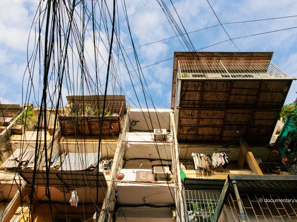 Bức ảnh chụp một toà nhà tập thể cũ với các ban công được bảo vệ bằng lưới sắt, dây điện chằng chịt phía trước. Hình ảnh gợi lên cảm giác hoài niệm về cuộc sống đô thị truyền thống tại Hà Nội.