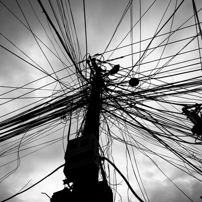 Bức ảnh chụp các dây điện chằng chịt trên cột điện trong một khu vực đô thị. Hình ảnh tạo cảm giác hỗn độn và phức tạp của hệ thống điện trong thành phố.