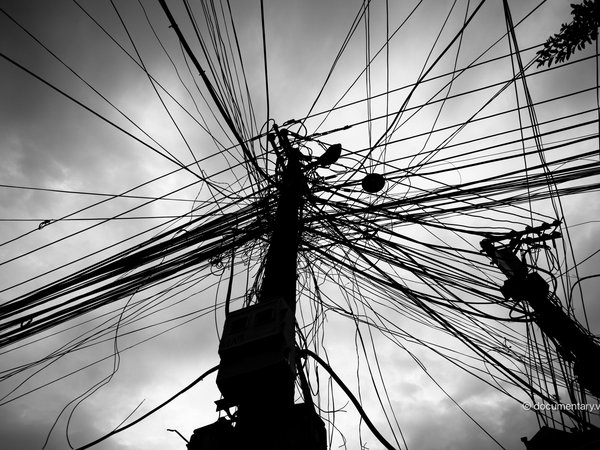 Bức ảnh chụp các dây điện chằng chịt trên cột điện trong một khu vực đô thị. Hình ảnh tạo cảm giác hỗn độn và phức tạp của hệ thống điện trong thành phố.