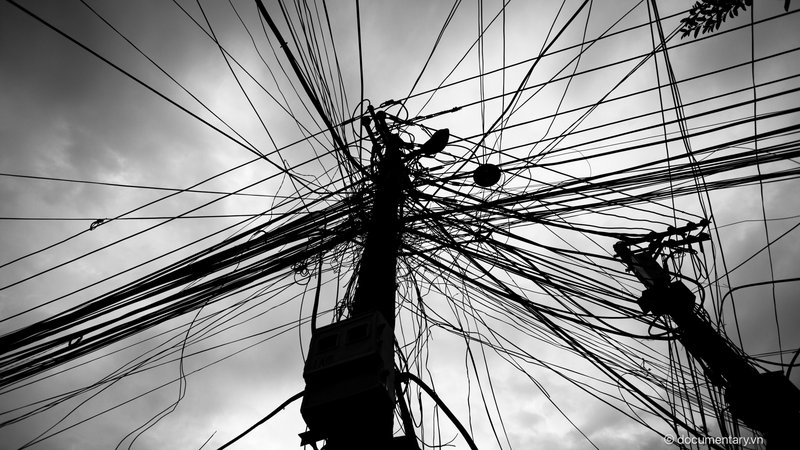 Bức ảnh chụp các dây điện chằng chịt trên cột điện trong một khu vực đô thị. Hình ảnh tạo cảm giác hỗn độn và phức tạp của hệ thống điện trong thành phố.