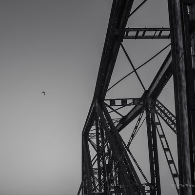 Hình ảnh thể hiện phần cấu trúc kim loại của cầu Long Biên với bầu trời rộng lớn phía sau và một con chim bay. Ảnh tạo cảm giác yên bình và tĩnh lặng, nhấn mạnh vẻ đẹp kiến trúc và không gian mở.