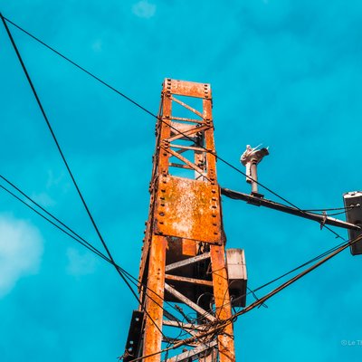 Hình ảnh một cột điện kim loại gỉ sét với nhiều dây điện căng ra xung quanh dưới bầu trời xanh. Bức ảnh tạo cảm giác yên bình và tĩnh lặng trong môi trường đô thị.