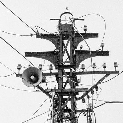 Bức ảnh chụp một cột điện với nhiều dây điện và một loa phường gắn trên đó. Hình ảnh tạo cảm giác bình dị và quen thuộc trong không gian đô thị.
