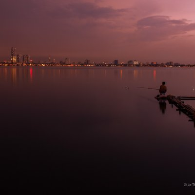 Bức ảnh chụp cảnh hoàng hôn trên Hồ Tây với hai người đang câu cá trên những chiếc bè nhỏ. Khung cảnh tạo cảm giác yên bình và tĩnh lặng với ánh sáng mềm mại của buổi chiều tà.