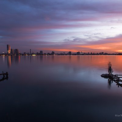 Bức ảnh chụp cảnh hoàng hôn trên hồ Tây với bầu trời rực rỡ màu sắc và phản chiếu trên mặt nước yên tĩnh. Cảnh vật mang lại cảm giác thanh bình và tĩnh lặng trong không gian đô thị.