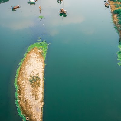 Bức ảnh chụp một đoạn sông với vài chiếc thuyền nhỏ neo đậu và một đảo nhỏ đất khô giữa dòng nước. Cảnh vật mang lại cảm giác yên bình và tĩnh lặng của vùng nông thôn vào ban ngày.