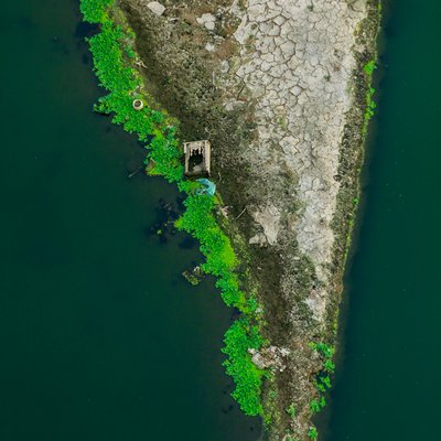 Ảnh chụp từ trên cao cho thấy một mảnh đất nứt nẻ bên bờ sông với thực vật xanh tươi bao quanh. Cảnh vật tạo cảm giác yên bình và tĩnh lặng.