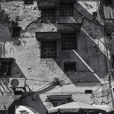 Bức ảnh chụp một bức tường cũ kỹ với ánh nắng xiên tạo ra các bóng đổ rõ nét. Cảnh vật mang lại cảm giác hoài niệm và yên bình về cuộc sống đô thị.