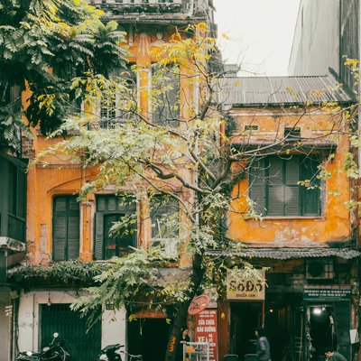 Bức ảnh chụp một ngôi nhà cũ với tường vàng sẫm và cửa sổ gỗ ở một con phố Hà Nội. Cảnh vật mang lại cảm giác hoài niệm về cuộc sống thường nhật nơi đô thị truyền thống.