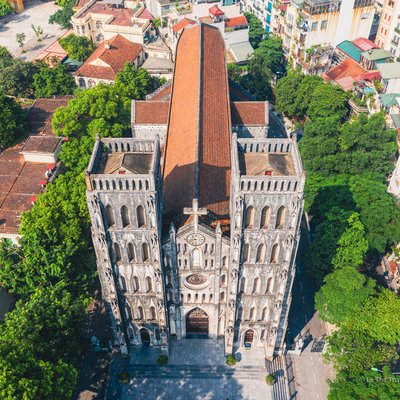 Hình ảnh chụp từ trên cao cho thấy Nhà thờ lớn Hà Nội với kiến trúc cổ kính và mái ngói đỏ nổi bật giữa khu vực đô thị xanh mát. Không gian yên tĩnh và ánh sáng ban ngày nhẹ nhàng tạo cảm giác thanh bình và tĩnh lặng.