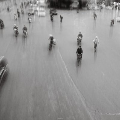 Bức ảnh chụp cảnh người dân đi xe đạp và xe máy trên đường phố Hà Nội với hiệu ứng mờ chuyển động. Hình ảnh tạo cảm giác nhịp sống đô thị năng động nhưng vẫn bình yên.