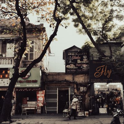 Bức ảnh chụp một góc phố Văn Miếu ở Hà Nội với những toà nhà cũ và cây xanh hai bên đường. Hình ảnh người bán hàng rong đội nón lá tạo nên cảm giác hoài niệm và bình dị về cuộc sống hàng ngày.