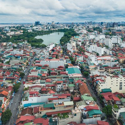 Ảnh chụp toàn cảnh khu phố cổ Hà Nội với hồ Hoàn Kiếm ở trung tâm, bao quanh bởi các toà nhà và mái nhà san sát. Bầu trời nhiều mây tạo cảm giác dịu nhẹ và yên bình cho cảnh quan đô thị này.