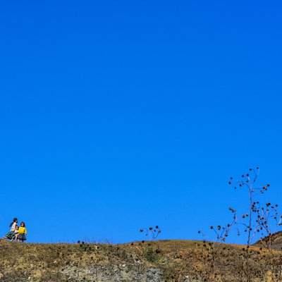 Bức ảnh chụp cảnh hai trẻ em đang đi trên đồi đất khô dưới bầu trời xanh trong vắt vào mùa xuân. Cảnh vật tạo cảm giác yên bình và tươi mới của vùng núi cao vào mùa xuân.