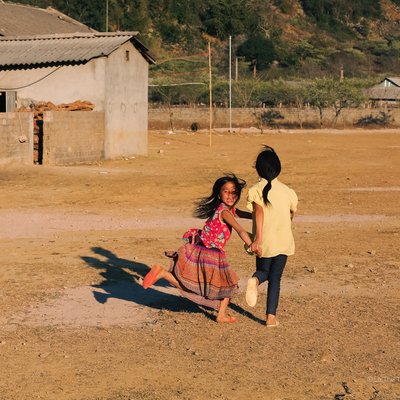 Bức ảnh chụp hai trẻ em đang chơi đùa ngoài trời ở vùng nông thôn Mộc Châu, Sơn La. Không khí trong ảnh tràn đầy năng lượng và sự vui tươi của tuổi thơ.