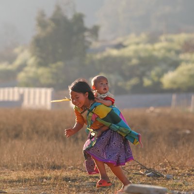 Bức ảnh chụp hai trẻ em đang vui chơi trên thảo nguyên vào mùa xuân tại vùng nông thôn. Cảnh vật mang lại cảm giác ấm áp và tràn đầy sức sống của tuổi thơ.