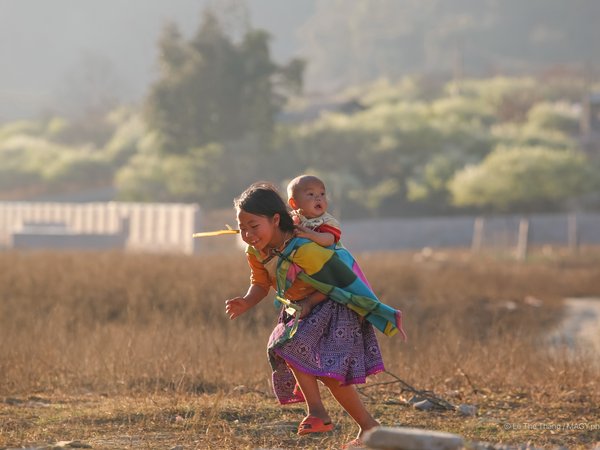 Bức ảnh chụp hai trẻ em đang vui chơi trên thảo nguyên vào mùa xuân tại vùng nông thôn. Cảnh vật mang lại cảm giác ấm áp và tràn đầy sức sống của tuổi thơ.