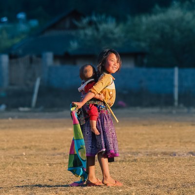 Bức ảnh chụp hai trẻ em ở Mộc Châu, Sơn La, trong một khung cảnh nông thôn với ánh sáng mềm mại buổi chiều. Hình ảnh tạo cảm giác bình yên và giản dị của cuộc sống thường ngày nơi đây.