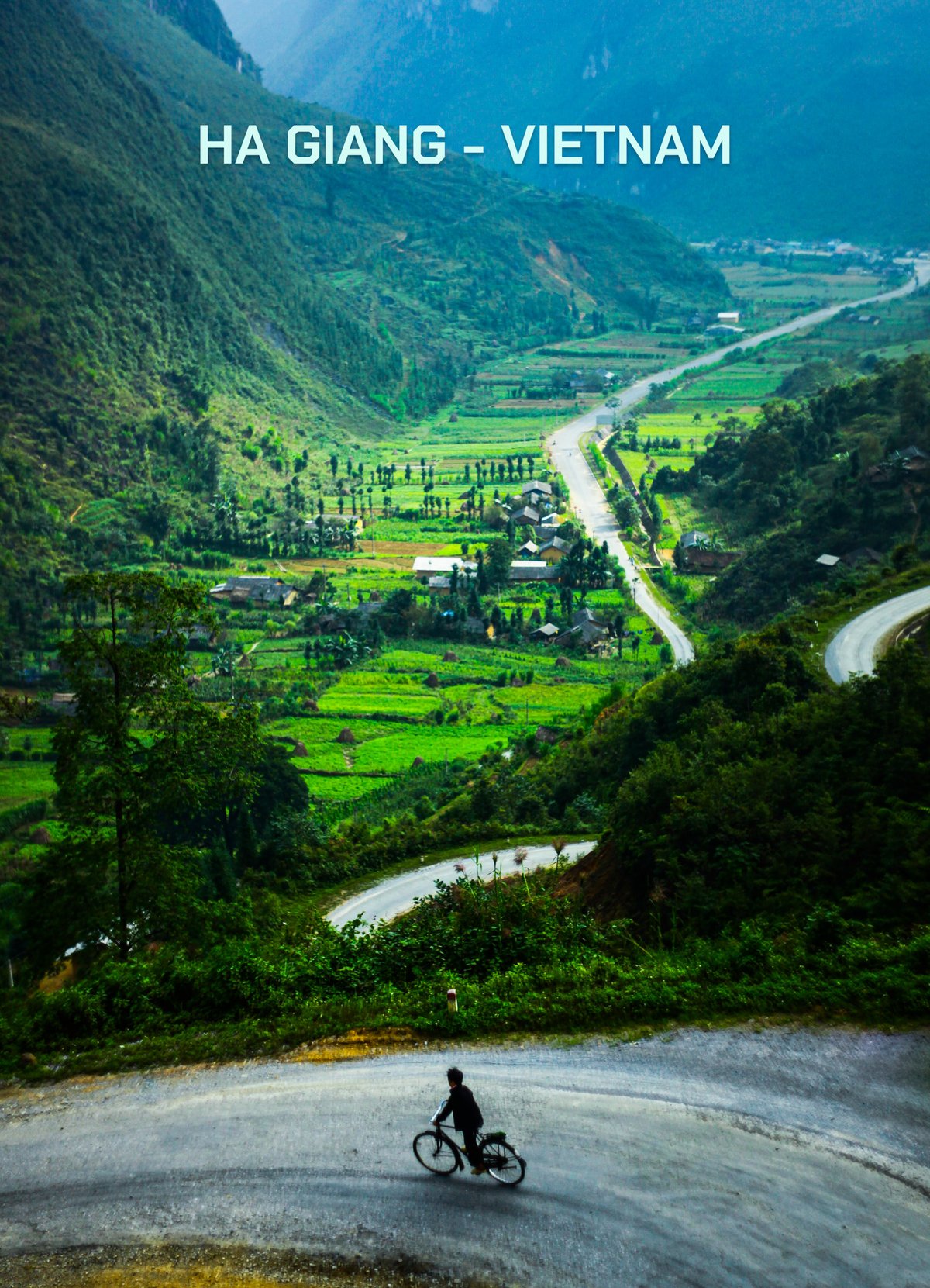 Bức ảnh chụp cảnh một người đang đạp xe trên con đường đổ dốc quanh co ở Hà Giang với cảnh quan núi non và thung lũng xanh mướt. Toàn cảnh tạo cảm giác yên bình và tĩnh lặng của vùng quê miền núi.