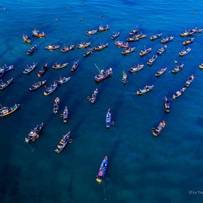 Hình ảnh chụp từ trên cao cho thấy nhiều tàu cá đang neo đậu trên biển tại chợ cá Tam Tiến, Quảng Nam. Cảnh tượng mang lại cảm giác yên bình và nhộn nhịp của một khu chợ truyền thống bên bờ biển.